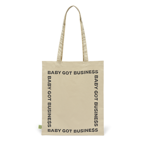Beigefarbene Stofftasche mit schwarzem Rundumdruck ‚BABY GOT BUSINESS‘ und kleinem grünem Smiley-Label an der Seite.