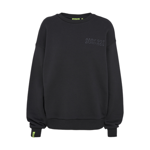 Schwarzer Oversized-Sweater mit Stickerei "BABY GOT BUSINESS" links auf der Brust und neon-grünem Markenlabel am Ärmel.